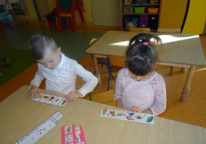 Dwoje dzieci rozwiązuje rebus fonetyczny.